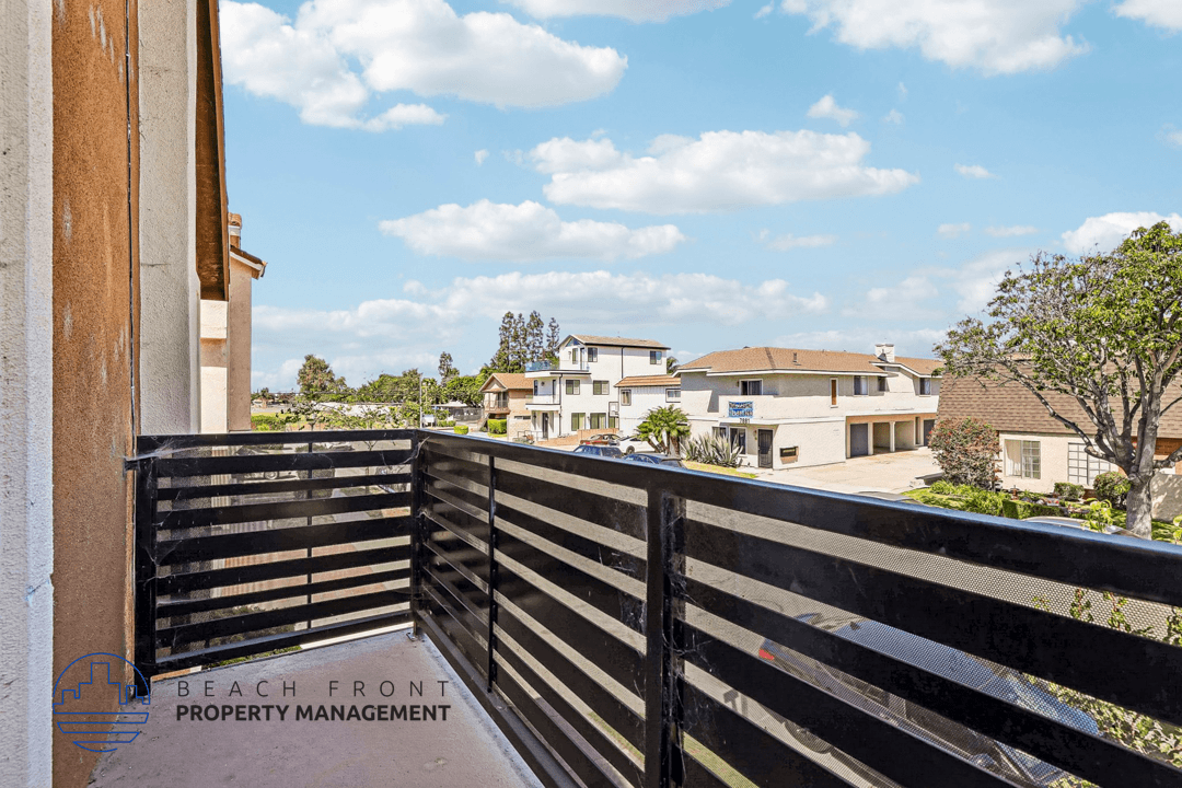 A balcony with a black railing overlooks a residential area.